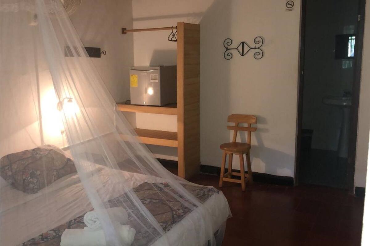 Un dormitorio con cama con dosel, una silla de madera, estante con un calentador y una puerta con letrero.