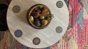 Een ronde tafel met een decoratieve schaal vol fruit en een houten lepel, omringd door versierde vloertegels.
