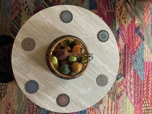 Een ronde tafel met een decoratieve schaal vol fruit en een houten lepel, omringd door versierde vloertegels.