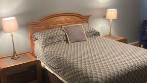 A bedroom with a wooden headboard, a quilted bedspread, two bedside lamps, and a nightstand. - Movie Matinee Hideaway  (Oklahoma City)