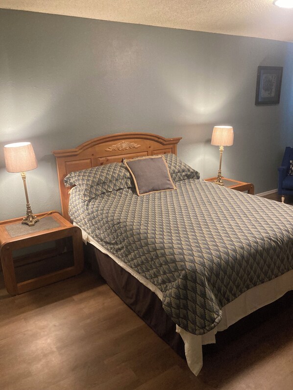 Een slaapkamer met een houten hoofdbord, een gewatteerde spreidekbed en twee bedlampjes op nachtkastjes.