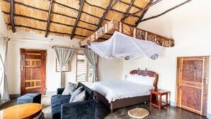 Una habitación con una cama, un sofá, una pequeña mesa y un techo de paja.