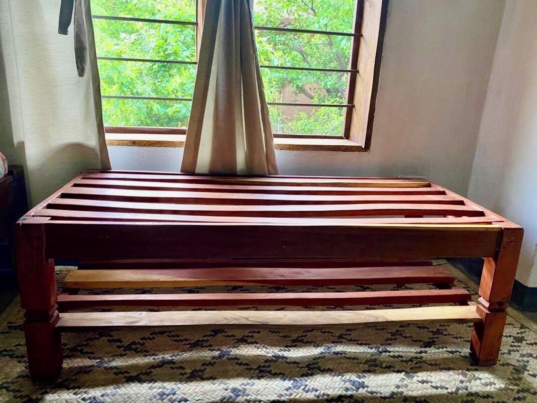 A wooden bench with a woven rug underneath, positioned in front of a window with a view of greenery.