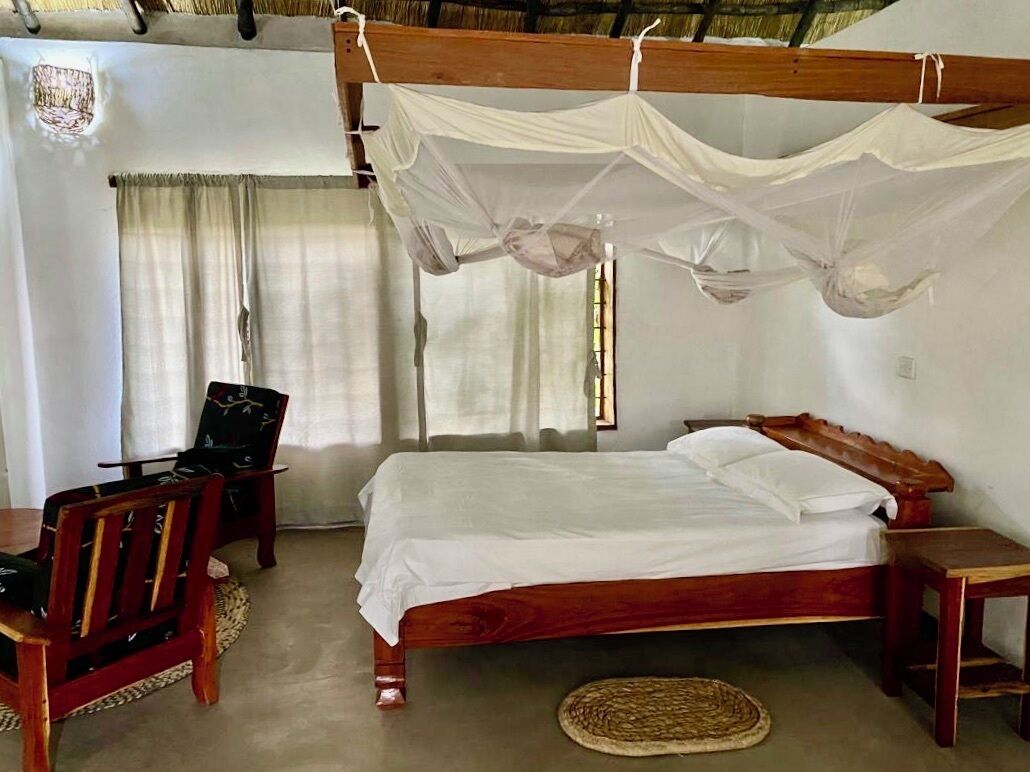 Una camera da letto con un letto e una sedia in legno, un comodino e una zanzariera sopra il letto.