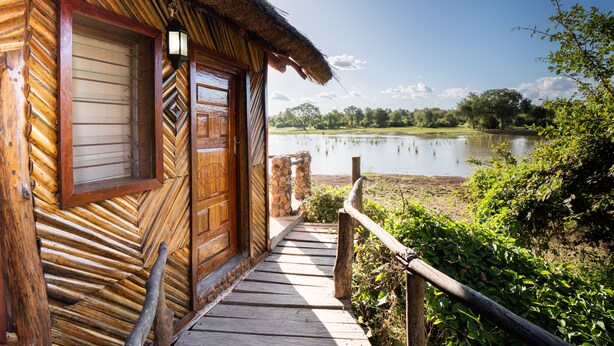 Una cabaña de madera con techo de paja, una terraza de madera que lleva a una puerta y vistas a un lago.