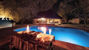Una piscina con hidromasaje y una zona de estar cubierta en la noche.