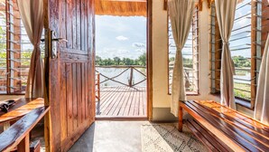 Puerta de madera que da a una terraza exterior con vista a un cuerpo de agua y vegetación.