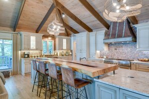 A spacious kitchen with a large island, wooden beams, and a stone backsplash.