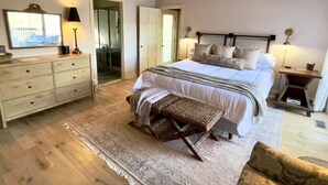Een slaapkamer met een groot bed, een houten bankje, een dressoir en een nachtkastje.