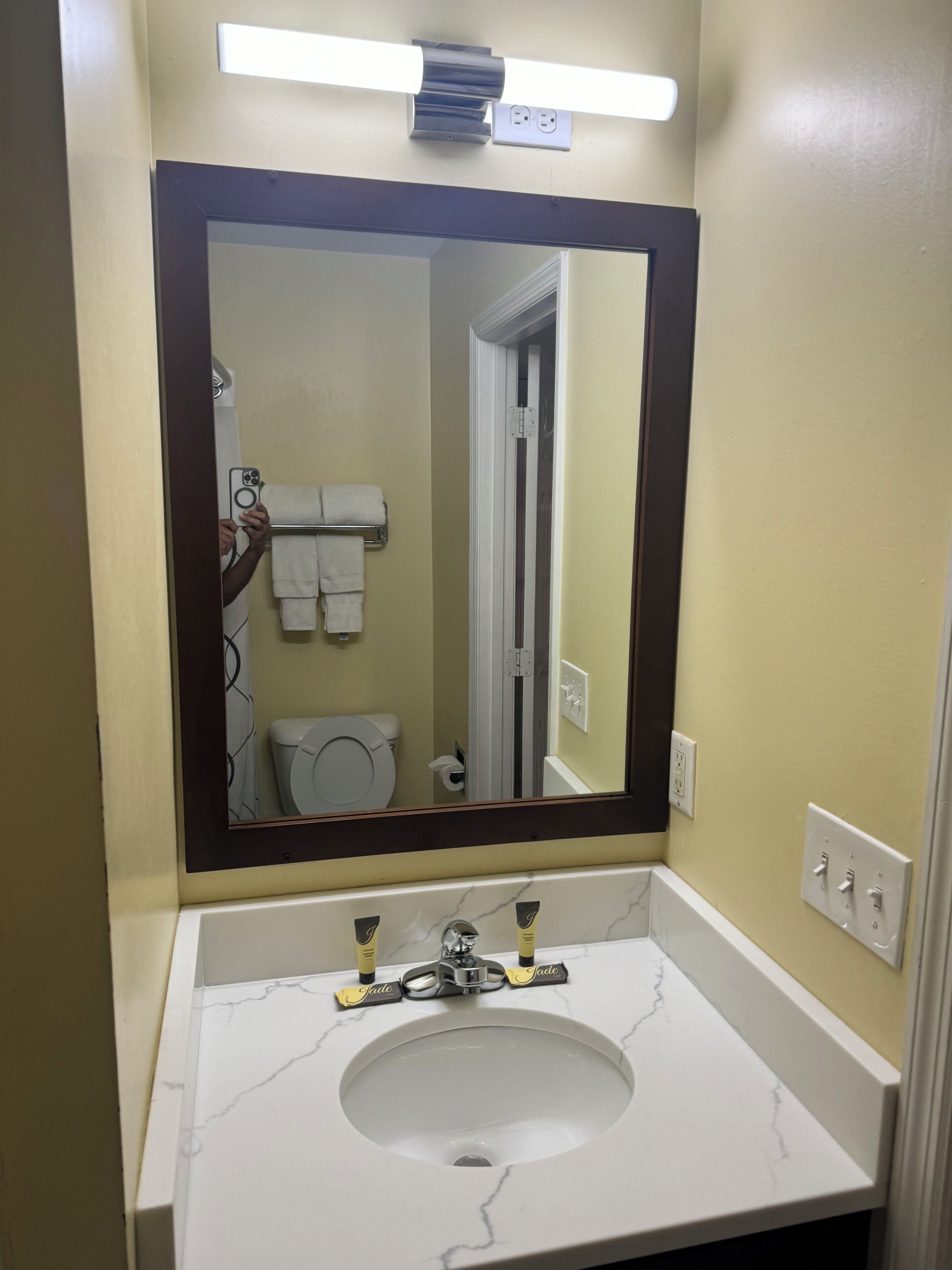 Un baño con un lavamanos blanco, un espejo grande y un perchero para toallas.