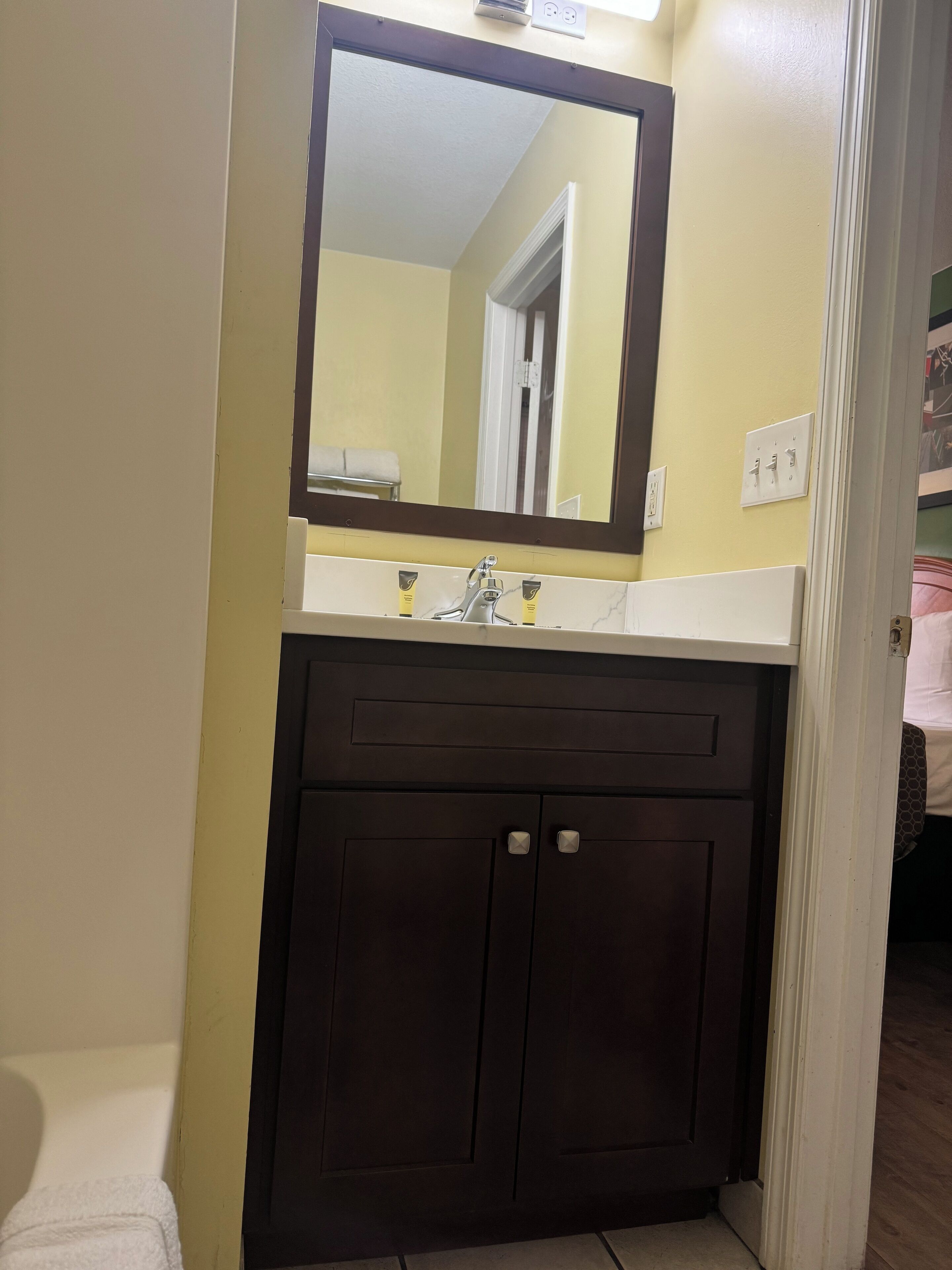 Un baño con tocador marrón oscuro, espejo y encimera blanca.