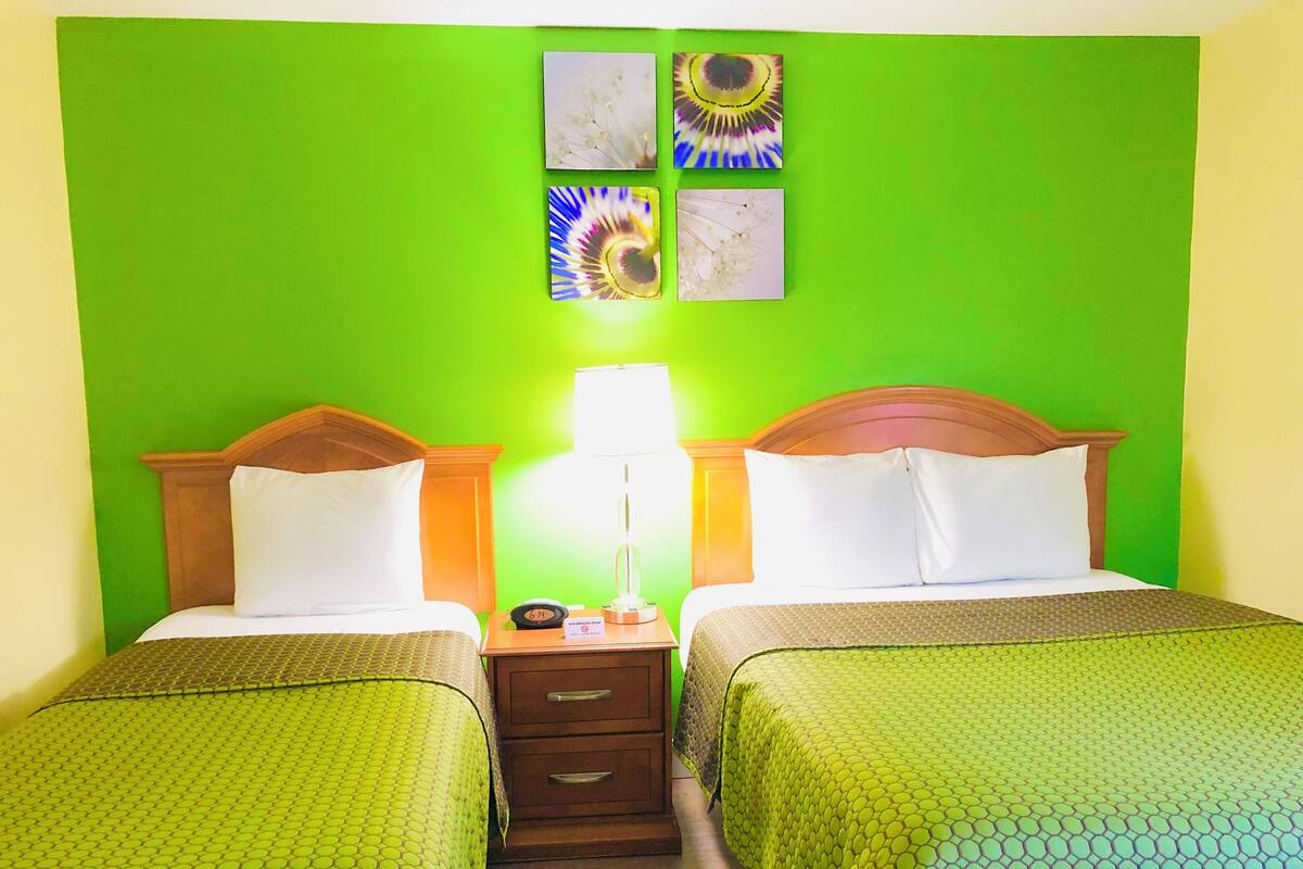 A hotel room with two beds, green walls, and a nightstand with a lamp and alarm clock.
