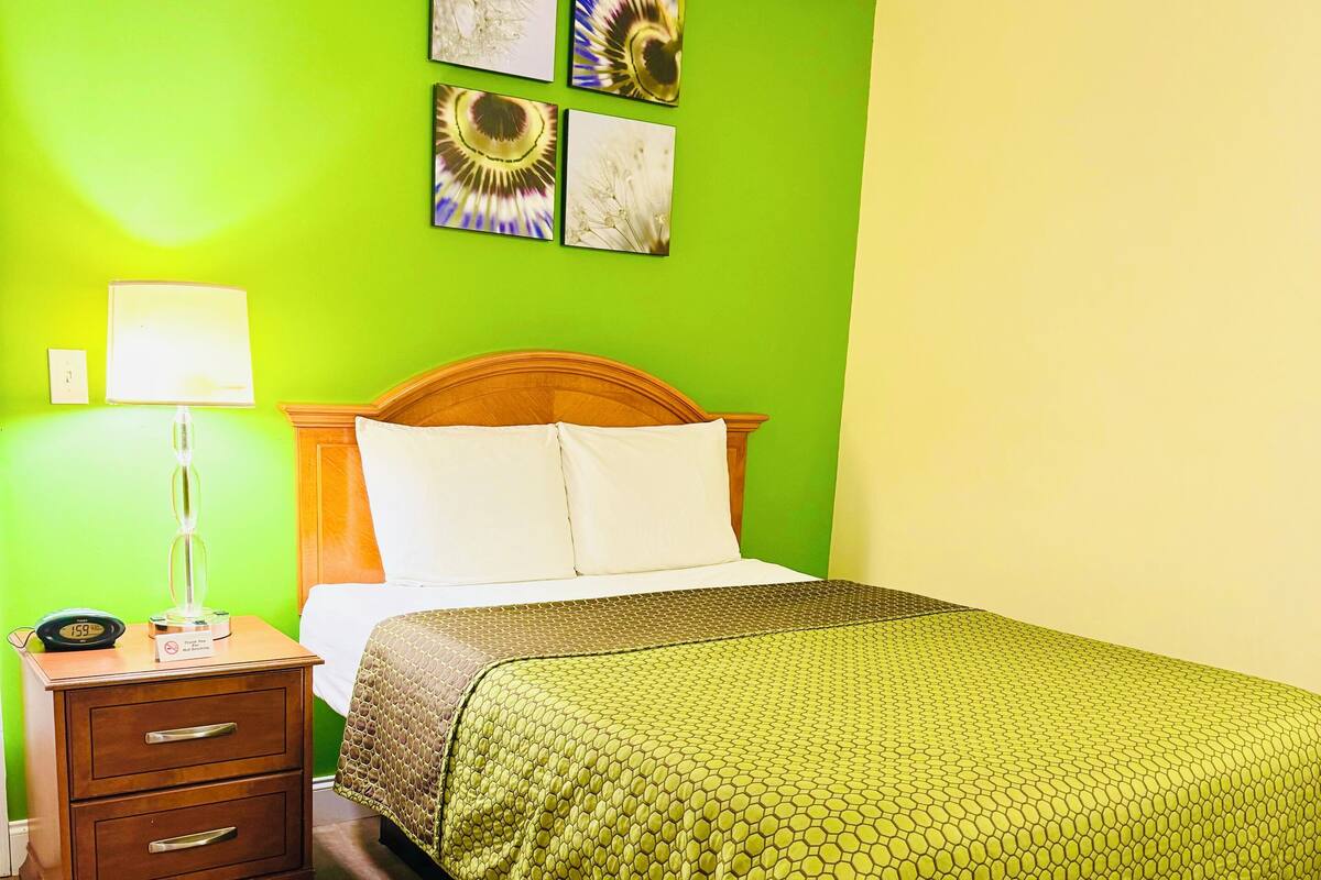 A room with a bed, a nightstand, a lamp, and a wall with four framed pictures.