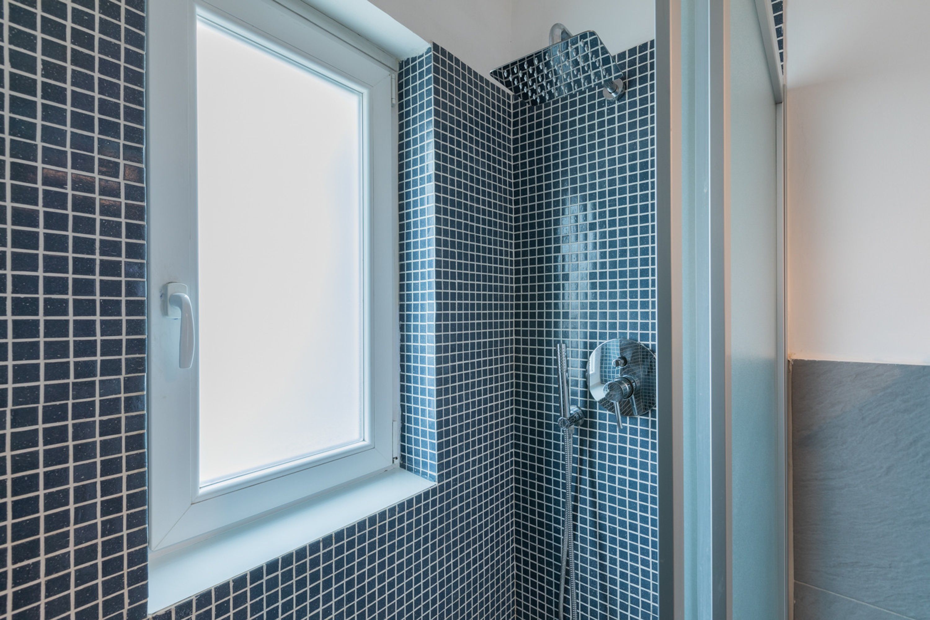 Une salle de bain avec une fenêtre, des murs carrelés et un espace douche.