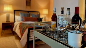 A hotel room with a bed, bedside lamps, a bedside table, and a tray with bottles and glasses.
