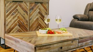 Ein Holztisch mit Fischgrätmuster, eine weiße Schale mit Snacks, zwei Gläser Weißwein und ein Teller mit Käse und Trauben.