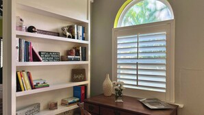 A room with a bookshelf, a desk, a window with blinds, and a decorative skull.
