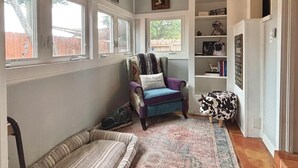 A cozy room with a window seat, a plush armchair, a decorative cow statue, and a bookshelf with dog-themed decor.