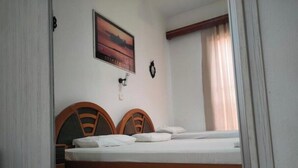 A bedroom with two wooden headboards, a bed with white linens, a wall-mounted light, and a framed picture above the bed.