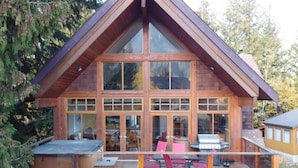 Una baita di legno con un'ampia veranda, un barbecue e un'area pranzo.