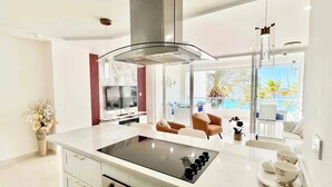 A modern kitchen with a central island, built-in oven, and a large window overlooking a balcony with outdoor seating.