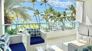 A balcony with wicker furniture, a view of the beach, and palm trees.