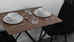 Une table à manger avec de l’assiette, des bols et des couverts blancs, placée devant un mur uni.