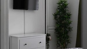 Une pièce avec une commode blanche, un téléviseur fixé au mur et une grande plante verte.