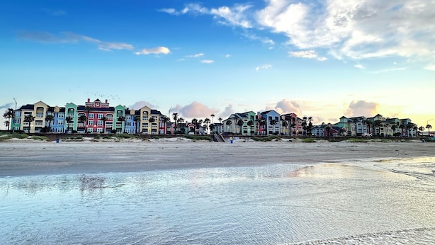 Un hotel frente a la playa con edificios coloridos, una playa de arena y olas.