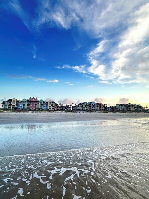 A beachfront hotel with colorful buildings, a sandy beach, and waves. - New rental. Clean. Steps to beach. Direct pool access. Close to everything. (Galveston)