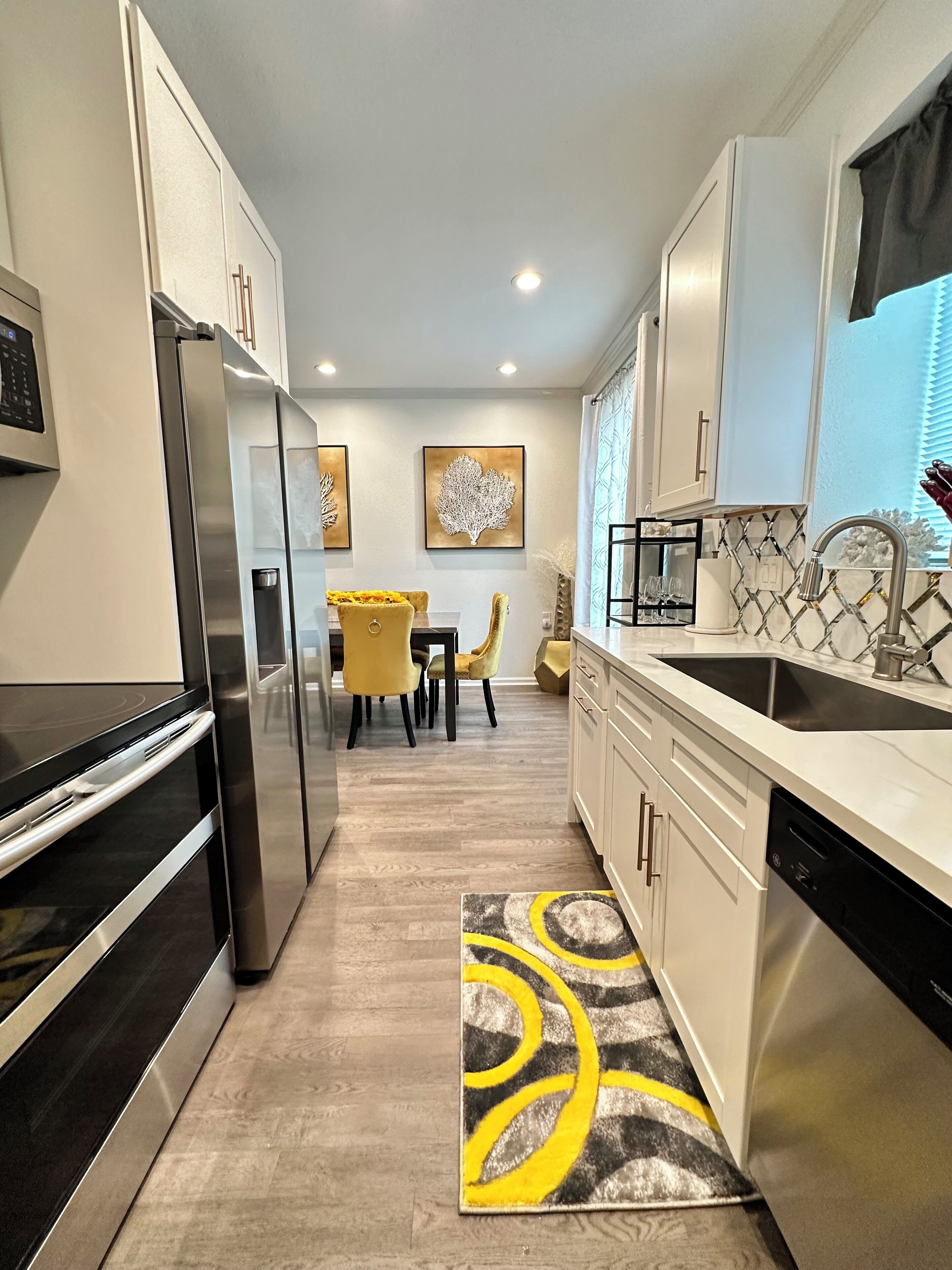 Une cuisine moderne dotée d’appareils électroménagers en acier inoxydable, un coin repas avec des chaises jaunes et un tapis à motifs.