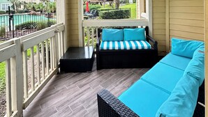 Un espacio de estar techado al aire libre con un sofá y una mesa, con vistas a una piscina y edificios.