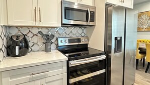 Una cocina moderna con gabinetes blancos, un microondas, estufa, horno y refrigerador de acero inoxidable.