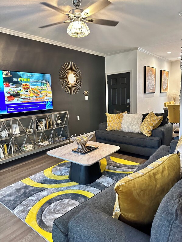A modern living room with a dark grey sofa, a coffee table, and a TV on the wall. - New rental. Clean. Steps to beach. Direct pool access. Close to everything. (Galveston)
