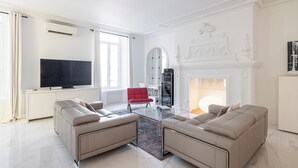 A modern living room with two beige sofas, a red chair, a glass coffee table, a flat-screen TV, and a fireplace. - Luxury Apartment BY Massena Square (Nice)