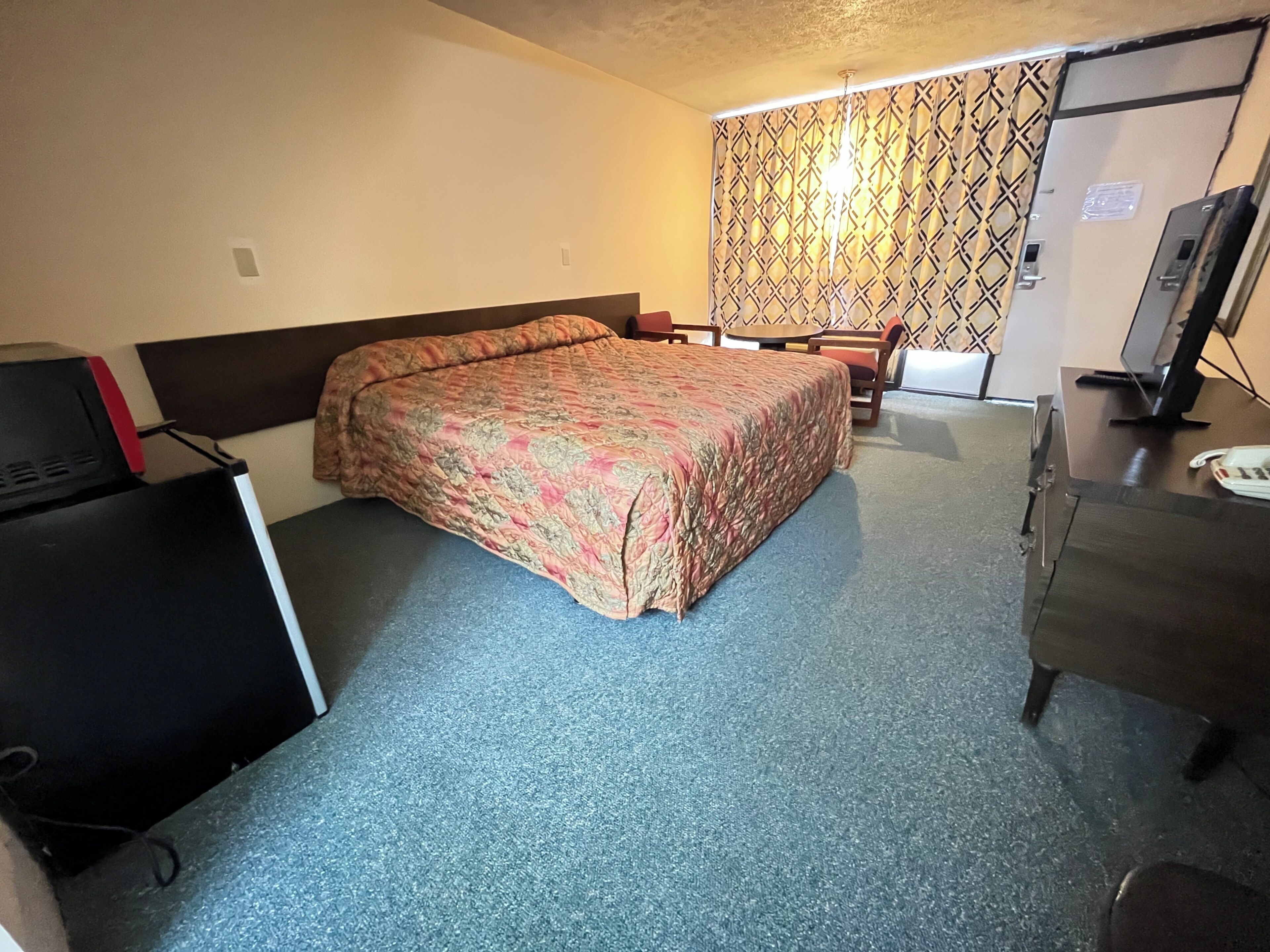 Una habitación de hotel con cama, escritorio, computadora, silla y televisor.