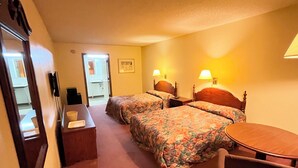Ein Hotelzimmer mit zwei Betten, einem Schreibtisch, einem Sessel und einem kleinen Tisch.