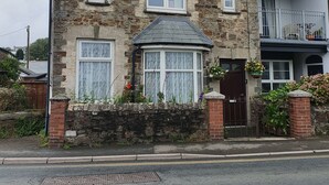 A stone building with multiple windows, a small porch, and a gated entrance. - Cosy light and spacious apartment in the heart of Stratton  (Stratton)