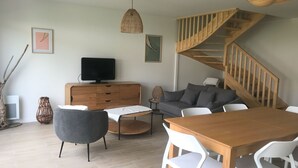 A modern living room with a wooden staircase, a dining table, and a sofa. - BETWEEN PINES AND OCEANS, IDEAL FOR FRIENDS AND FAMILY (Léon)