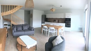 A modern living space with a staircase, a sofa, a dining table, and a kitchen area. - BETWEEN PINES AND OCEANS, IDEAL FOR FRIENDS AND FAMILY (Léon)