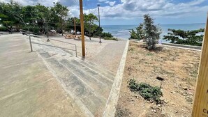 Une zone dallée avec des tables et des bancs pour pique-niquer, un petit arbre et une vue sur la mer.