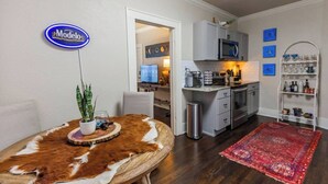 Eine moderne Küche mit weißen Schränken, einer Mikrowelle und einer Kaffeemaschine. Es gibt einen Essbereich mit einem runden Tisch und einem roten Teppich.
