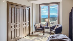 A room with a large window offering a mountain view, a door with a decorative panel, two chairs, a small table, and a fluffy rug. - The Timbers by Okanagan Premier (Beaverdell)