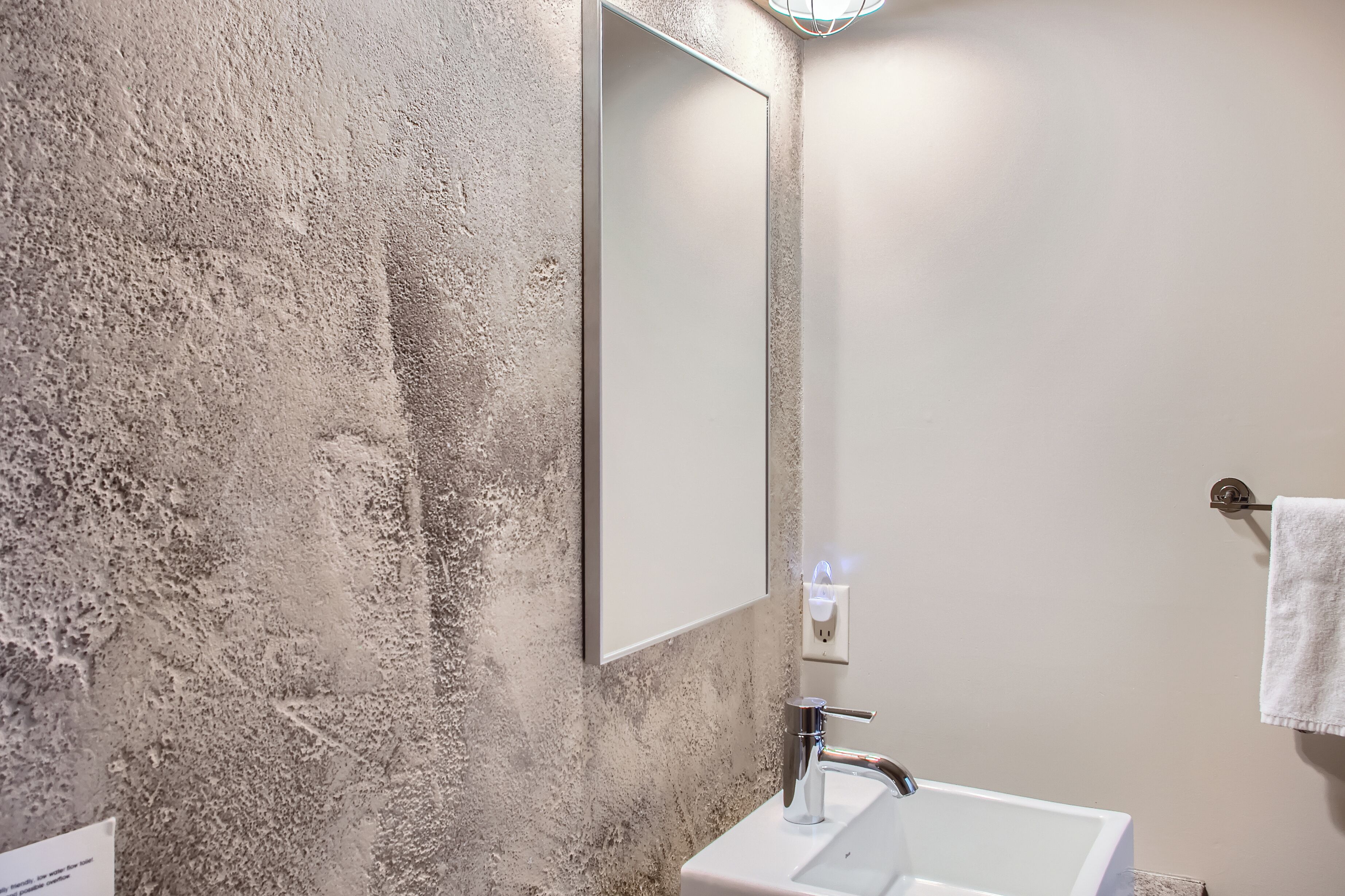 Un baño con pared texturizada, un lavamanos blanco, un espejo y una toalla colgada en un perchero.
