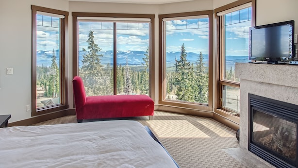 A bedroom with a large bed, a red chair, a fireplace, and a TV. - The Timbers by Okanagan Premier (Beaverdell)