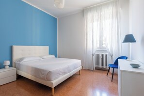 A bedroom with a bed, a nightstand, a desk, a chair, and a window with curtains. - Appartamento Ibisco by Wonderful Italy (Bologna)