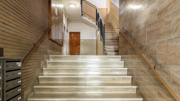 Una escalera con barandilla de madera y peldaños color beige que conducen a una puerta en la parte superior.