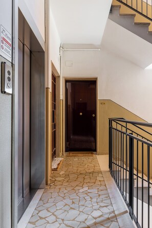 A hallway with a stone floor, a door, and a staircase with a metal railing. - Appartamento Ibisco by Wonderful Italy (Bologna)