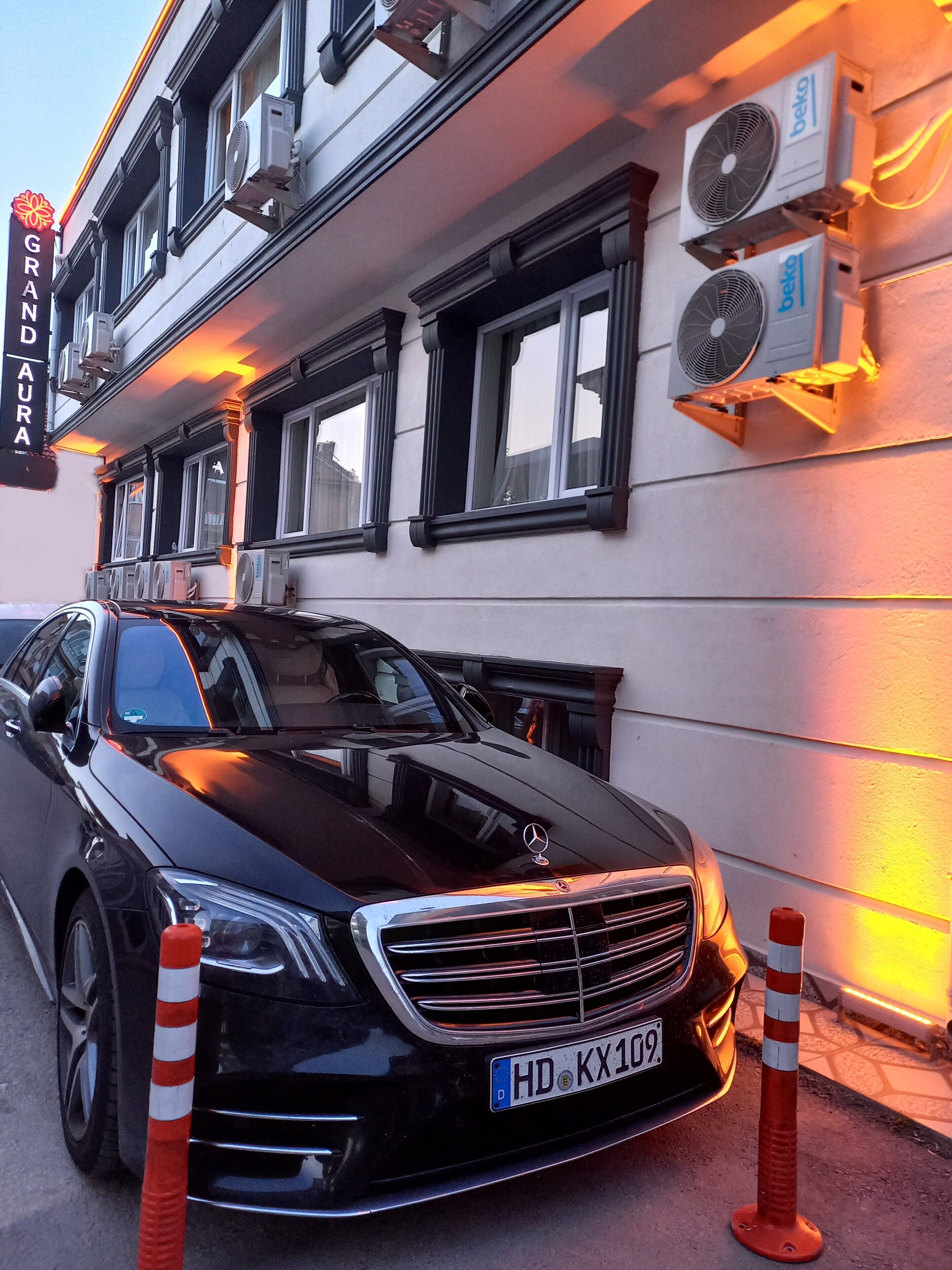 Een zwarte Mercedes-Benz geparkeerd voor een gebouw met een bord waarop 'GRAND AURA' staat.