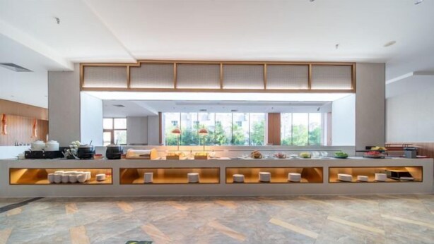 A modern hotel lobby with a central reception desk, built-in shelves, and a large window offering a view of greenery. - Yulong Hotel (Wusu)